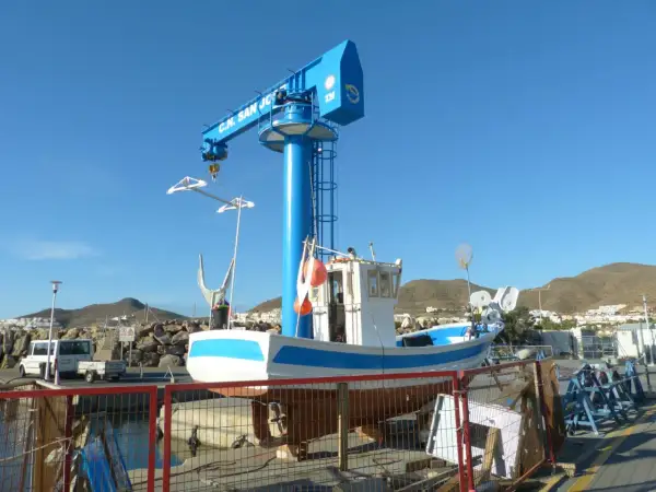 Barco pesquero blanco y azul en dique seco, bajo una grúa azul con "C.N. San José" escrito.