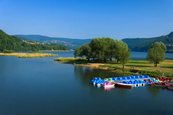 Jezioro Żywieckie, z kolorowymi rowerami wodnymi przy brzegu, otoczone zielonymi wzgórzami. Głębokość jeziora zachęca do wodnych zabaw.