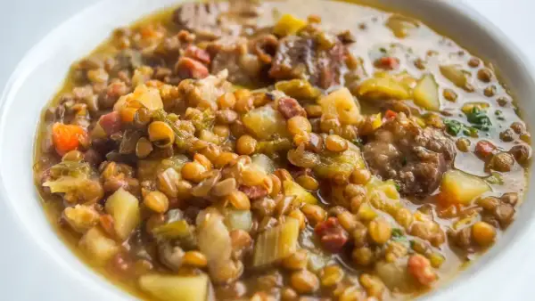 Un plato reconfortante de lentejas con trocitos de sobrasada, patatas y verduras en un caldo sabroso.