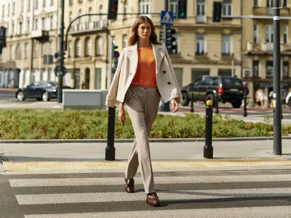 Elegancka kobieta prezentuje stylizacje do beżowego płaszcza, idąc przez pasy.