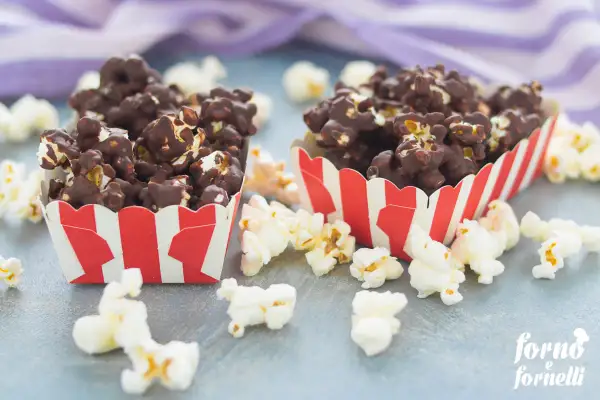 Due contenitori a righe rosse e bianche pieni di pop corn al cioccolato, perfetti per scoprire come fare i pop corn al cioccolato.