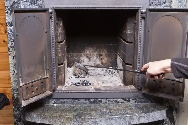 Maintenant, que faire de la suie de cheminée ? Une main utilise une pince pour nettoyer les cendres et la suie d'un foyer ouvert.