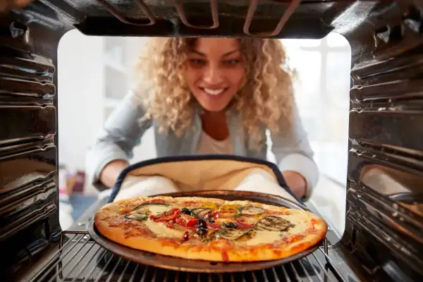 Uśmiechnięta kobieta wyjmuje z piekarnika pyszną pizzę. Idealna temperatura do pieczenia pizzy to klucz do sukcesu.