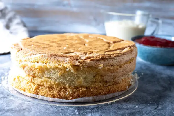 En gyllene tårtbotten, redo för ett tårtbotten recept. Bredvid står en skål med sylt och en kanna med grädde.