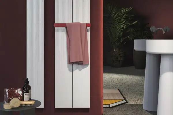 Termosifoni elettrici: pro e contro. Due radiatori bianchi verticali con un asciugamano rosa appeso. Un bagno moderno con piante e lavabo.