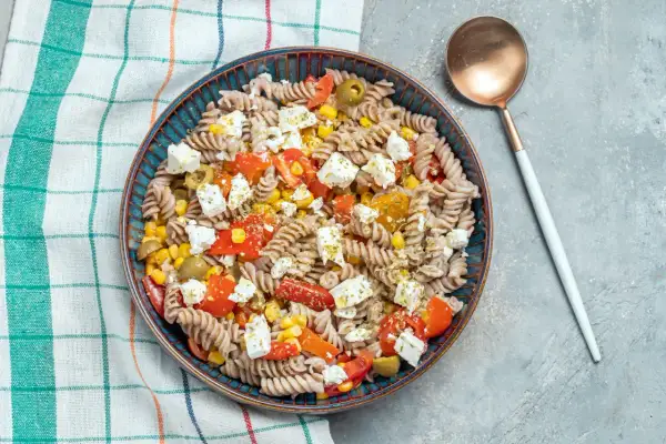 Insalata di pasta integrale con pomodorini, mais, olive e feta. Un condimento pasta per dieta leggero e gustoso.