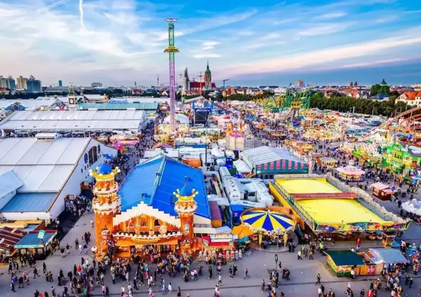 Aerial view of a crowded Oktoberfest fairground with tents, rides, and people.