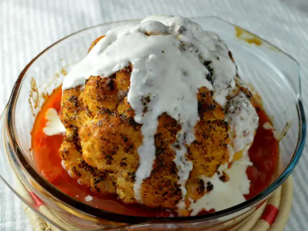 Hel blomkål i ugn, gyllene och kryddad, badar i en smakrik tomatsås och toppas med en krämig sås. En festlig rätt!