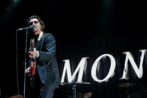 Alex Turner w okularach przeciwsłonecznych śpiewa i gra na gitarze podczas jednego z koncertów Arctic Monkeys.
