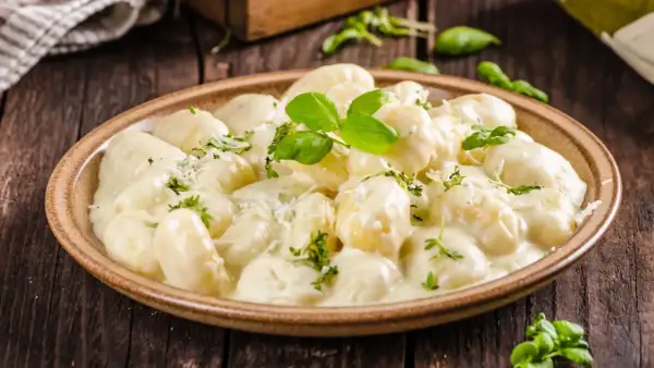 Pyszne gnocchi z kurczakiem w kremowym sosie, posypane parmezanem i świeżą bazylią. Idealne danie na obiad.