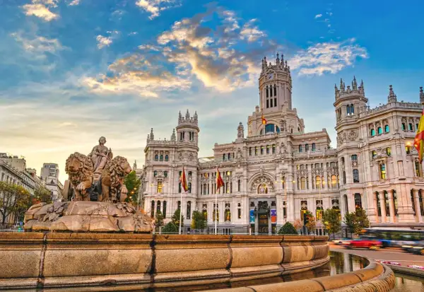 Cibelesfontänen framför det ståtliga Palacio de Comunicaciones, ett ikoniskt konstmuseum i Madrid, under en dramatisk solnedgång.