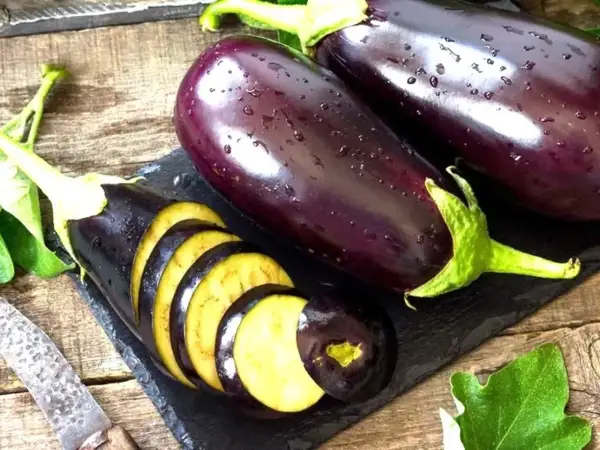 Berenjenas frescas, una cortada en rodajas, mostrando su interior amarillo. ¡Se puede comer la berenjena cruda!