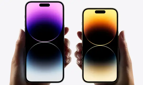 Dwie dłonie trzymają telefony iPhone 16. Jeden z nich ma fioletowy ekran, drugi złoty.