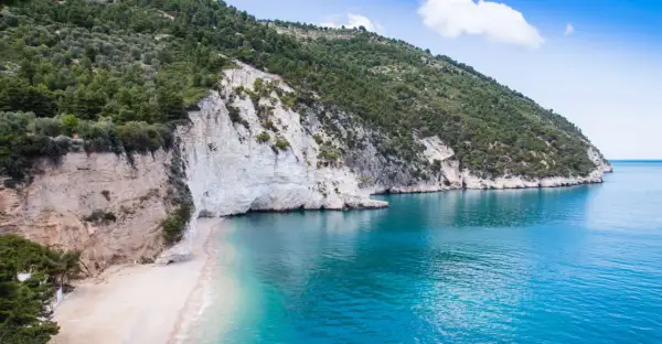 Spiaggia di Vignanotica, con scogliere bianche a picco sul mare turchese e una collina verdeggiante.