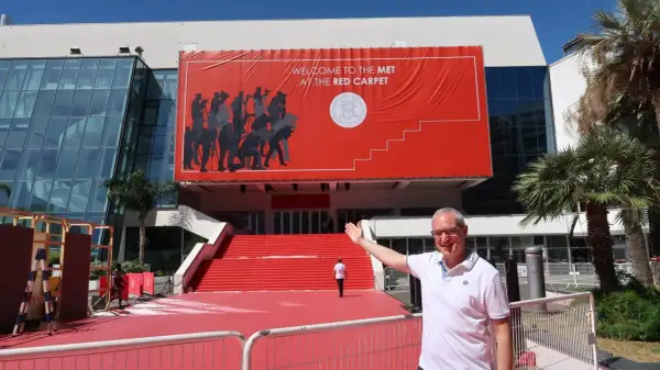 Mężczyzna pozuje przed budynkiem z wielkim czerwonym banerem "Welcome to the Met at the Red Carpet". To przygotowania do festiwalu w Cannes.