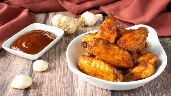 Alette di pollo croccanti e dorate, appena sfornate dalla friggitrice ad aria, servite con salsa barbecue e aglio.