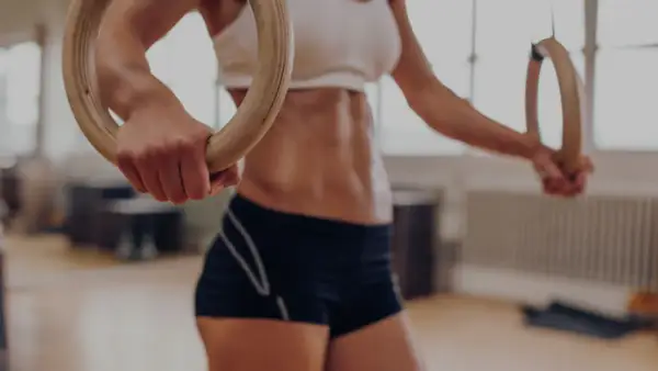 Kobieta z wyrzeźbionym brzuchem ćwiczy na kółkach gimnastycznych, przygotowując się do wyzwań crossfitu.