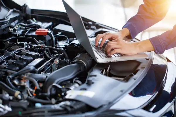 Mechanik diagnozuje brak mocy na ciepłym silniku benzyna, używając laptopa do analizy danych z jednostki napędowej.