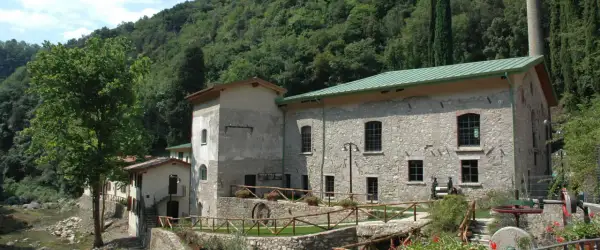 Antica cartiera toscolano immersa nel verde, con un ruscello che scorre e un antico mulino a vista.