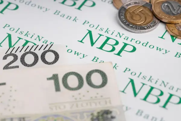 Polskie banknoty 100 i 200 zł oraz monety na tle dokumentu NBP. Symbolizują finanse, w tym odsetki od zaległości podatkowych.
