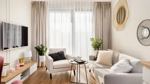 Przytulny salon w stylu minimalistycznym. Jasna kanapa, fotel, stolik kawowy i telewizor tworzą harmonijną przestrzeń.