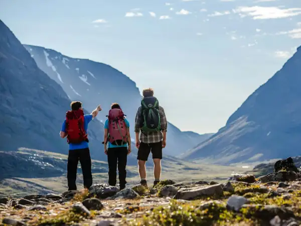 Två vandrare med ryggsäckar blickar ut över en dalgång i Abisko. En pekar mot bergen.