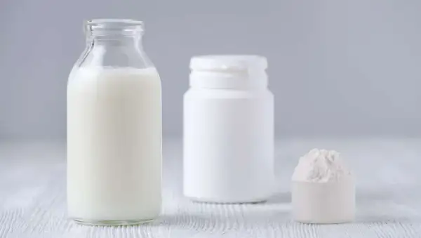 Bottiglia di latte, contenitore bianco e misurino con polvere. Le proteine del latte si trovano in questi prodotti.
