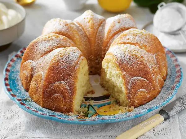 En saftig sockerkaka med yoghurt, pudrad med florsocker, serverad på en vacker blå tallrik.