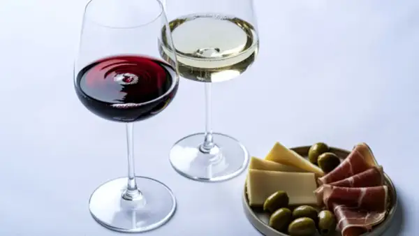 Dwa kieliszki wina, czerwonego i białego, z deską serów, oliwek i szynki. Wino właściwości są doceniane przez koneserów.