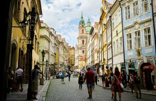 Rue pavée bordée de maisons colorées à Prague, avec une église baroque au loin. Une scène typique du top 10 des attractions de Prague.