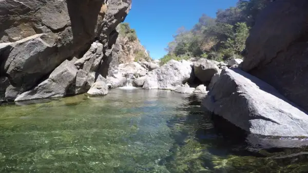 Agua cristalina en la charca de las nutrias, rodeada de rocas y vegetación bajo un cielo azul.