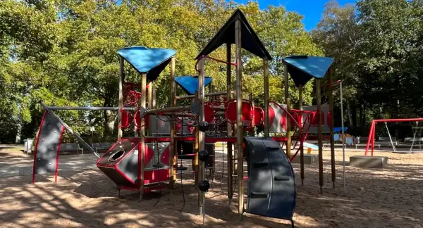 Ein bunter Spielplatz mit Klettergerüst und Schaukeln in einem der Wuppertal Parks, umgeben von Bäumen im Herbstlicht.