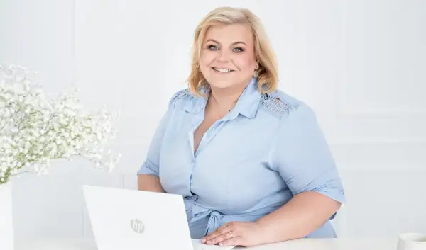Uśmiechnięta kobieta przy laptopie, gotowa pomóc w znalezieniu pracy w Wielkiej Brytanii.