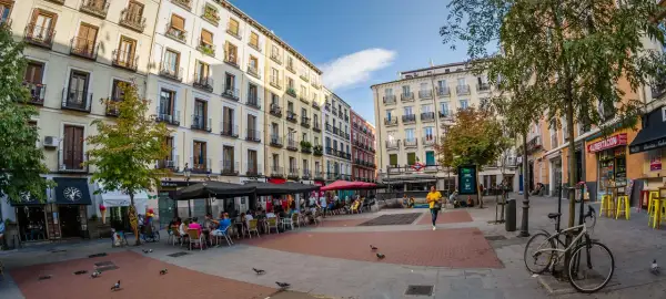 Piazza vivace con caffè all'aperto e persone che passeggiano, un'atmosfera tipica della zona gay di Madrid.