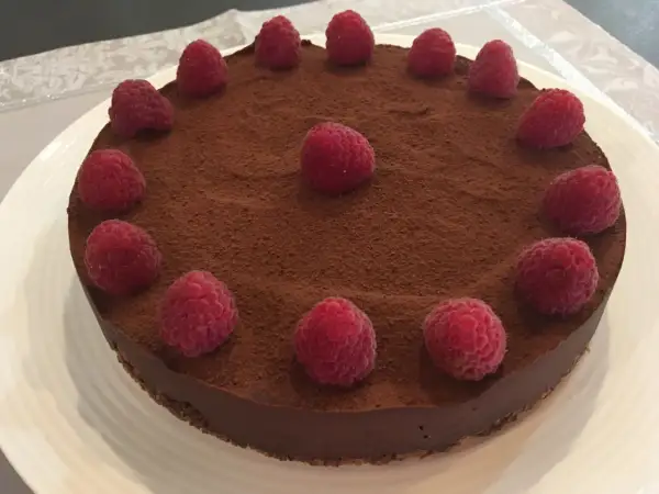 Tarte chocolat framboise, une gourmandise visuellement irrésistible, saupoudrée de cacao et ornée de framboises fraîches.