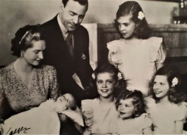 Familjefoto med prinsessan Sibylla och hennes barn. Bilden visar en familj med föräldrar och flera barn, inklusive en bebis. Prinsessan Sibylla bar en mönstrad klänning.