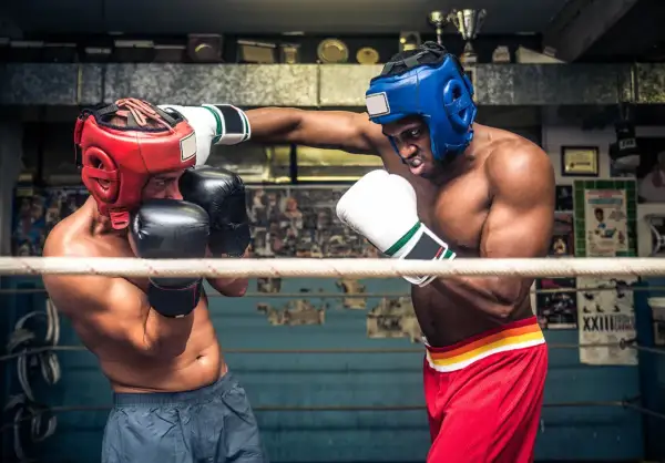 Två boxare i ringen, en med röd och en med blå hjälm, tränar funktionell fitness.