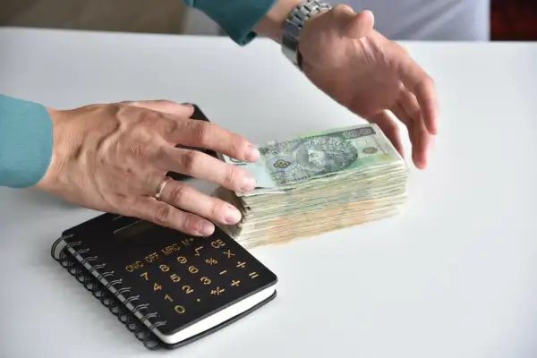 Ręce liczą stos banknotów, obok kalkulator. Jak odzyskać pieniądze z banku po zmarłej osobie?