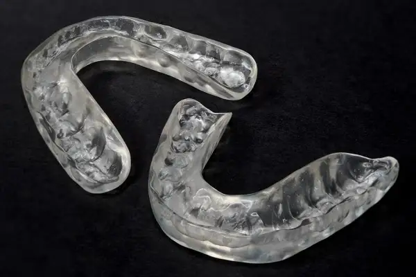 Due bite occlusali trasparenti, sagomati per adattarsi all'arcata dentale, su sfondo nero.