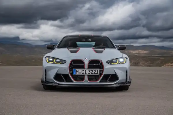 Szare BMW M4 CS z czerwonymi akcentami i agresywnym grillem, gotowe do jazdy po pustynnej drodze pod burzowym niebem.