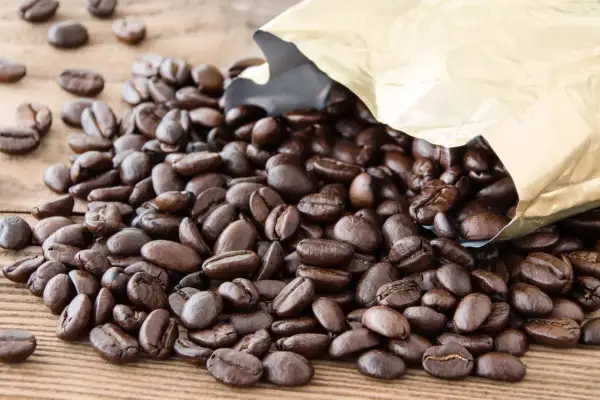 Chicchi di caffè Arabica tostati, con un sacchetto dorato aperto da cui fuoriescono. Il caffè Arabica, noto per il suo aroma delicato, è il significato di un'esperienza gustativa raffinata.