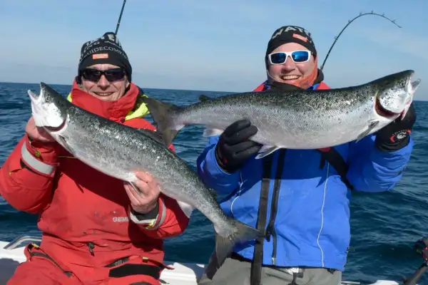 Zwei Angler auf einem Boot zeigen stolz ihre gefangenen Lachse. Ein toller Fang, der zeigt, wo man Lachs angeln kann!