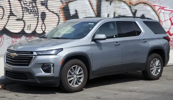 Szary Chevrolet Traverse SUV zaparkowany przed ścianą z graffiti.