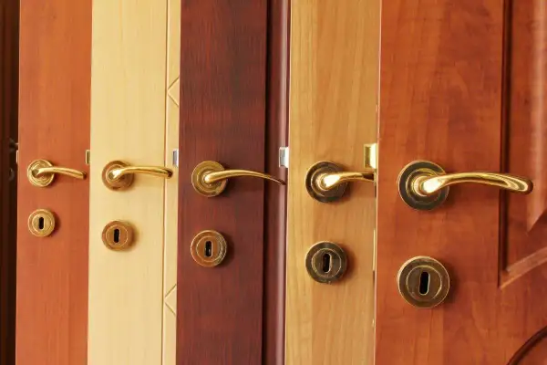 Plusieurs portes en bois aux teintes variées, chacune ornée d'une poignée dorée. L'idée de peindre une porte en bois prend tout son sens devant cette diversité.