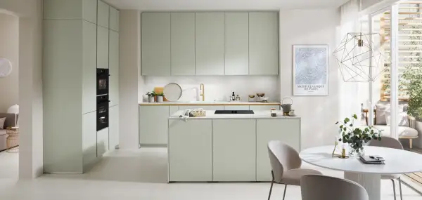 Moderna cocina verde con isla central, electrodomésticos integrados y una mesa redonda con sillas.