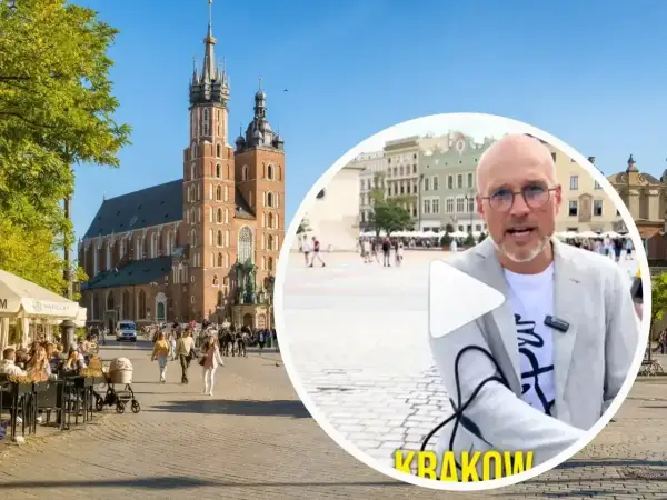 Mężczyzna w okularach opowiada o tym, czy jest krakow safe, na tle Rynku Głównego z Kościołem Mariackim.