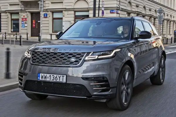 Szary Range Rover Velar jedzie ulicą w mieście. Kierowca jest widoczny za kierownicą.