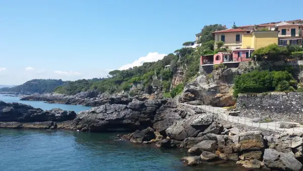 Case colorate su una scogliera rocciosa, con il mare blu e il cielo limpido. Un sentiero panoramico si snoda lungo la costa, ricordando la bellezza della riviera delle palme San Benedetto del Tronto.