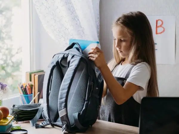 Dziewczynka wkłada książkę do plecaka. Zastanawia się, jak prać plecak w pralce, by był czysty na nowy rok szkolny.