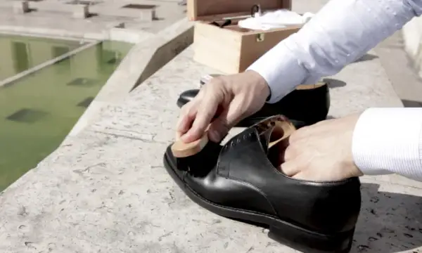 Un homme prend soin de ses chaussures noires, appliquant du cirage avec une brosse. La fréquence du cirage chaussure est essentielle pour leur longévité.